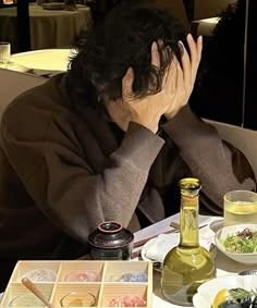 a man sitting at a table with food and drinks in front of him, covering his face