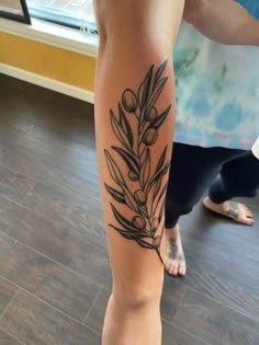 a woman's leg with an olive branch tattoo on it