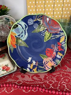 a blue plate with flowers on it sitting on a red tablecloth next to other dishes