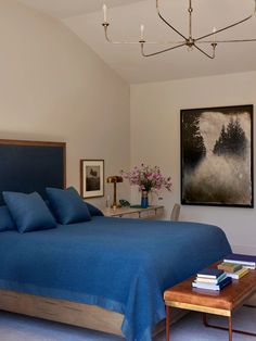 a bed with blue sheets and pillows in a bedroom next to a painting on the wall