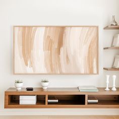 an abstract painting hangs on the wall above a wooden shelf with books and vases