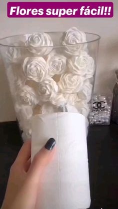 a person holding a roll of toilet paper in front of a vase filled with white roses