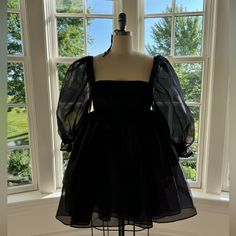 a mannequin is standing in front of a window wearing a black dress with sheer sleeves