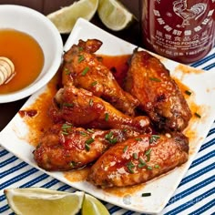 some chicken wings are on a plate next to a bowl of honey and limes