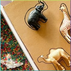 two toy animals are sitting on top of a piece of cardboard with an elephant and giraffe