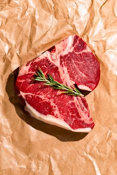 two pieces of raw meat sitting on top of brown paper with green sprigs