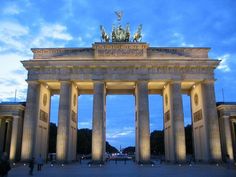 people are walking around in front of an arch with statues on it at night time