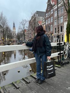 a woman is standing on a bridge looking at the water and buildings in the background