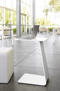 an open laptop computer sitting on top of a white table next to a chair and ottoman