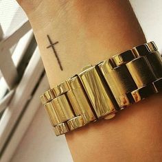 a gold bracelet with a cross tattoo on the wrist is shown in front of a window