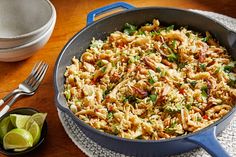 a skillet filled with rice and vegetables next to a bowl of lime wedges