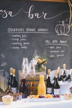 a table with bottles of wine and glasses on it next to a chalkboard sign