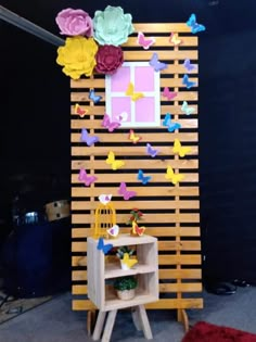 a wooden wall with paper flowers and butterflies on the top, next to a shelf