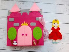 a pink felt castle with a princess doll next to it on a white wooden surface