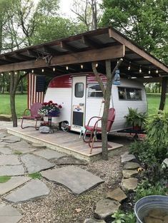 an rv is parked under a covered area in the yard with chairs and tables around it