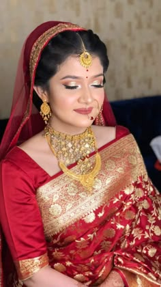 a woman in a red and gold sari with jewelry on her neck, looking down at the ground