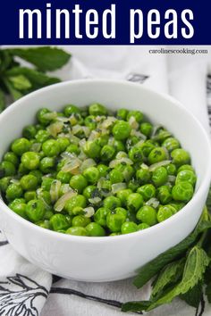 a white bowl filled with green peas on top of a table next to mint leaves