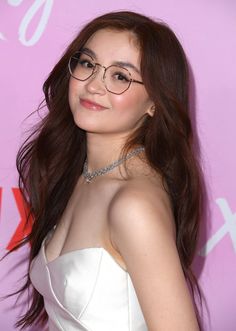 a woman wearing glasses standing in front of a pink background