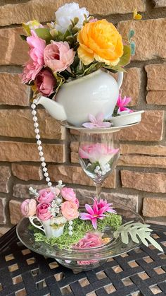 a vase filled with flowers sitting on top of a glass plate next to a brick wall