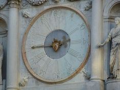 a large clock mounted to the side of a stone building with statues on either side