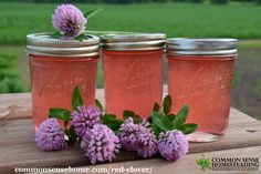 three mason jars filled with pink flowers sitting on top of a wooden table in front of a field