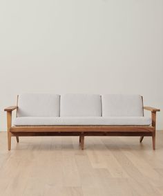 a wooden couch sitting on top of a hard wood floor next to a white wall