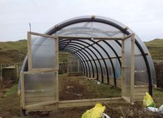 a large metal and wood greenhouse in the middle of an open field with plastic bags around it