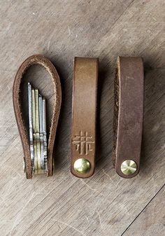 three different types of leather bookends on a wooden table with metal bells and pencils in them