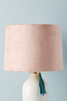 a white table lamp with a pink shade on the top and green tassels