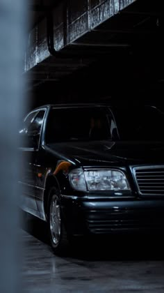 a black mercedes benz parked in a dark parking garage with its hood up and lights on