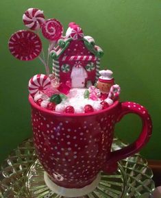 a cup filled with candy and candies on top of a glass table next to a green wall