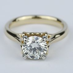 a yellow gold engagement ring with a round cut diamond in the center, on a white background