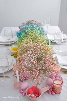 a table topped with lots of different colored candies and flowers in vases next to white plates