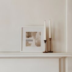 two candles are sitting on a mantle with a framed photograph and candle holder next to it