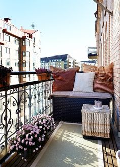 an apartment balcony with lots of furniture and pillows on the top floor, along with flowers