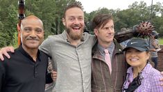 three men and one woman are posing for a photo with their arms around each other