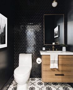 a white toilet sitting next to a wooden cabinet in a black and white tiled bathroom