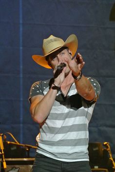 a man wearing a cowboy hat and holding his hands in the air while standing on stage