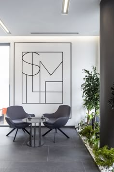 two chairs and a table in an office with plants on the wall behind them,