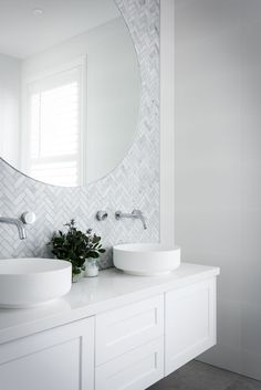 a bathroom with two sinks and a large round mirror above the sink, along with a plant on the counter