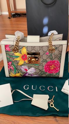 New Authentic GUCCI Flora HandBag with gold color Metallic Padlock and Keys. Ebony color Leather. Suede Lining inside with 2 pockets. Detailed Flower design. Fun and Gorgeous Bag. Dust bag included and Gucci shopping bag. Chain drop 11". Orig Price $2200+tax Gold Top Handle Box Bag With Branded Hardware, Gold Box Bag With Branded Hardware And Top Handle, Designer Gold Box Bag With Double Handle, Designer Satchel With Gold-tone Hardware, Designer Shoulder Bag With Gold-tone Hardware For Daily Use, Designer Gold Shoulder Bag For Daily Use, Multicolor Travel Bags With Branded Hardware, Travel Bags With Branded Hardware In Multicolor, Designer Gold Shoulder Bag With Top Carry Handle