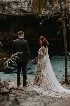 a bride and groom holding hands while standing in front of a waterfall at their wedding