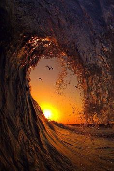 the sun is setting behind an ocean wave with birds flying over it and water splashing