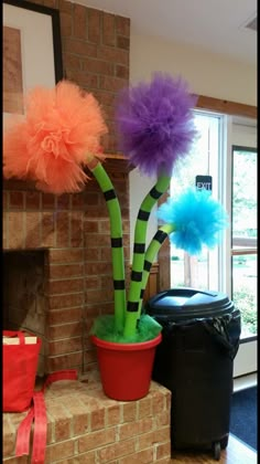 two fake flowers in a pot on top of a brick fireplace with tissue pom poms