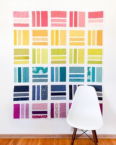 a white chair sitting in front of a wall with a colorful quilt hanging on it