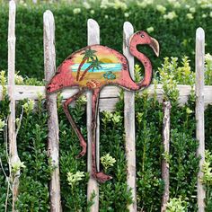 a flamingo painted on the side of a wooden fence in front of bushes and shrubbery