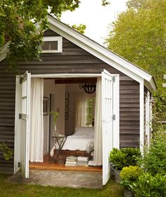 a small shed with a bed in it and curtains on the door, next to some trees