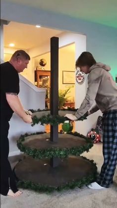 two men are decorating a christmas tree with fake greenery on the top and bottom