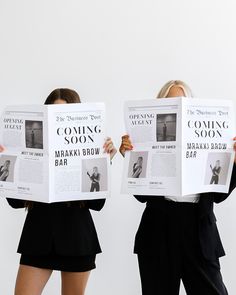 two women in business attire hold up newspapers