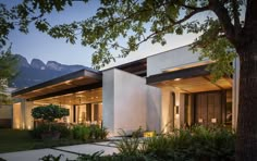 an exterior view of a modern house with trees in the foreground and mountains in the background